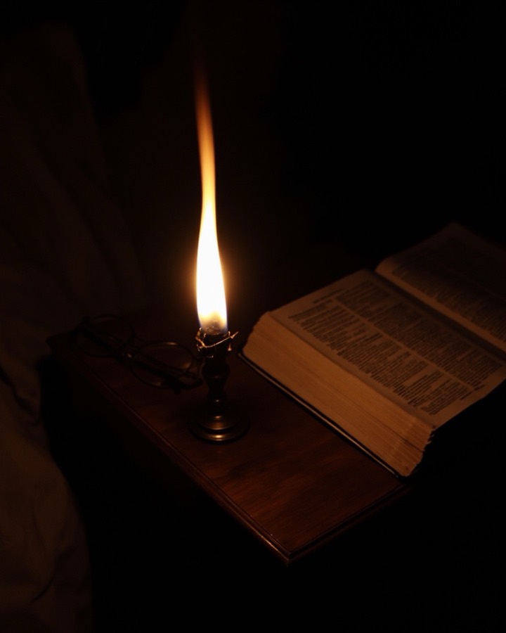 An oil lamp burning beside an open Bible at night